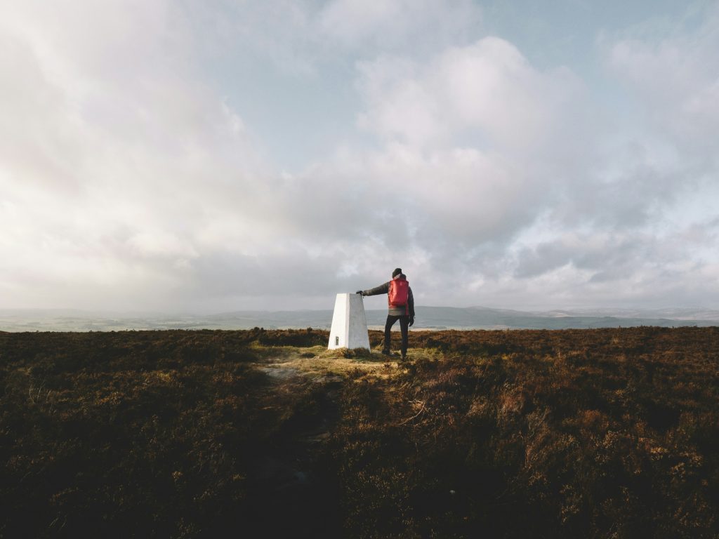 hiker standing on hillside looking across peaceful countryside landscape