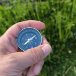 hiker holding a compass while navigating a countryside trail