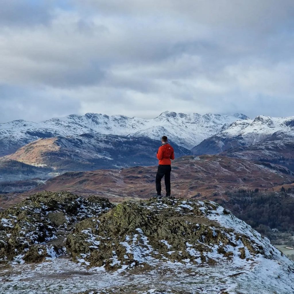 hiker standing on rocky hill UK mountains winter snow landscape