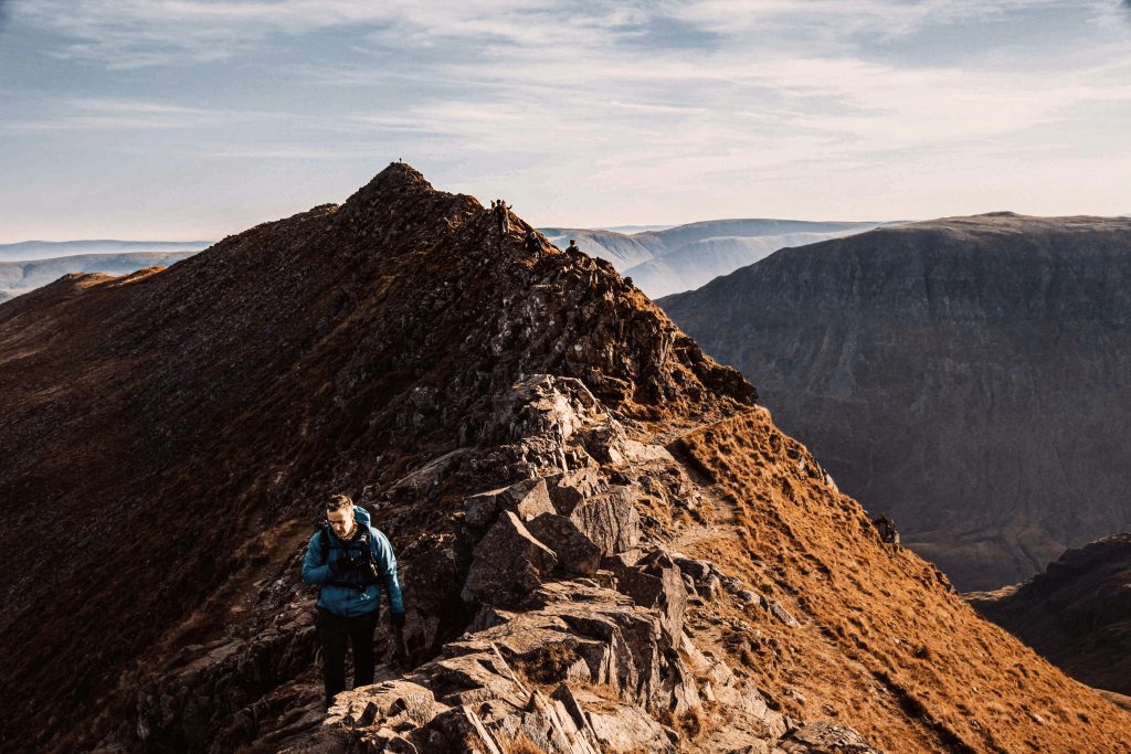 Hiker climbing the narrow rocky ridge of Striding Edge on Helvellyn, Lake District