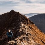 Hiker climbing the narrow rocky ridge of Striding Edge on Helvellyn, Lake District